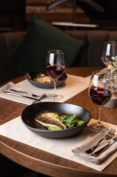 Sült tengeri sügér petrezselyemmel és avokádóval fekete tányéron, romantikus vacsora részeként egy étteremben.  - Fotó, kép