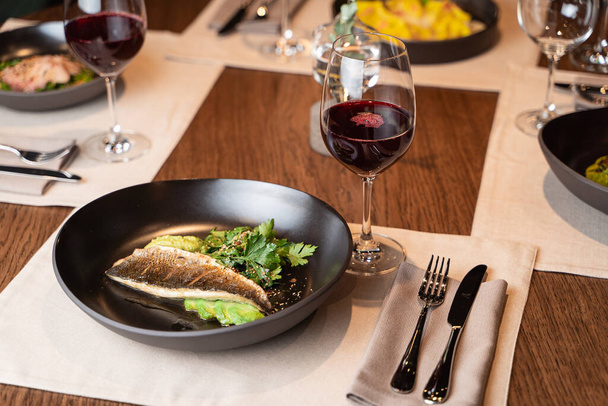 Branzino arrosto con prezzemolo e avocado su un piatto nero, servito come parte di una cena romantica in un ristorante
  - Foto, immagini