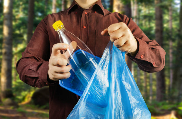 Photo of a man in brown shirt disposing plastic bottle and can in bag protecting forest environtment. - Photo, image