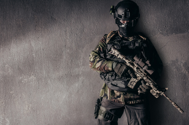 Photo of a fully equipped soldier in camouflage uniform standing on grungy concrete wall background. - Foto, Imagen