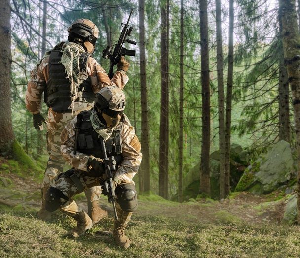 Foto van een volledig uitgeruste soldaten in outfit, harnas, helm, bril met automatisch geweer poseren op bosachtergrond. - Foto, afbeelding