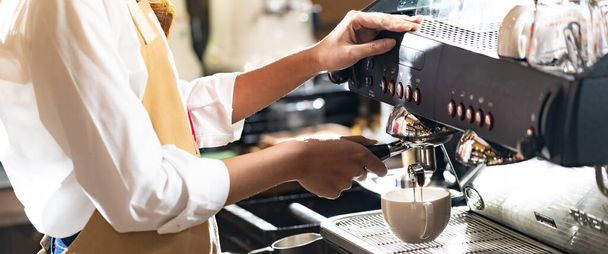 Close-up shot of a barista brewing coffee by modern coffeemaker machine to making a cup of coffee with other barista working. Using for small business entrepreneur owner, Panorama web banner crop. - Photo, Image