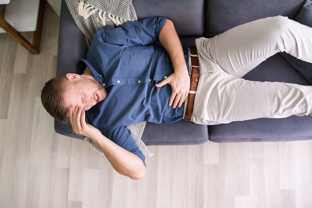 Man Suffering From Stomach Ache Lying On Sofa - Foto, immagini