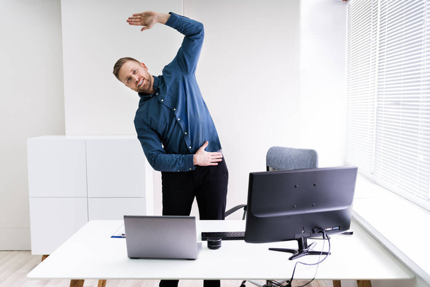 Young Businessman Doing Stretching Exercise In Office - Photo, image