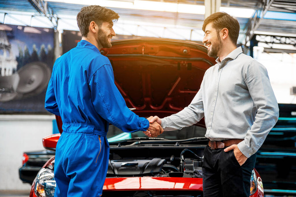 The mechanic shaking hands with customer after finish checking the opened hood red car. Focus on happy mechanic and satisfied customer. Auto car repair service center. Professional service. - Foto, imagen
