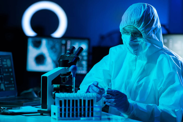 Scientist in protection suit and masks working in research lab using laboratory equipment: microscopes, test tubes. Coronavirus 2019-ncov hazard, pharmaceutical discovery, bacteriology and virology - Valokuva, kuva