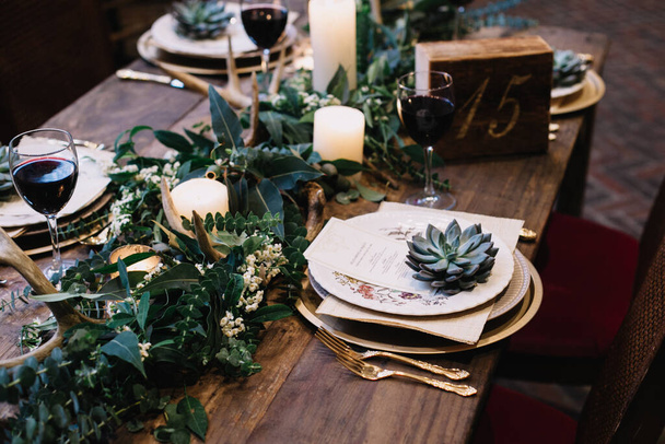 Eski plakalı kırsal düğün masası, yeşil ve beyaz okaliptüs çelengi, geyik boynuzu, altın kaplar. Boho tarzı. Bir etkinlik, parti, tarih ya da düğün için masa hazır. Kırmızı şarap. - Fotoğraf, Görsel