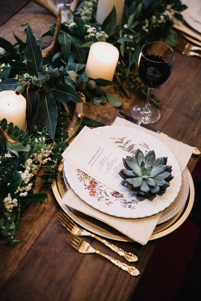 Mesa de boda rústica con platos vintage, guirnalda de eucalipto verde y blanco, astas de ciervo, utensilios de oro. Estilo boho. Juego de mesa para un evento, fiesta, fecha o boda. Vino tinto servido
 - Foto, imagen