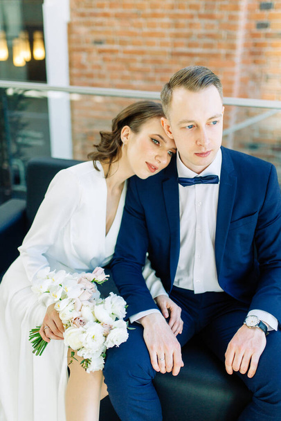 The bride and groom's romantic photo shoot. The newlyweds are happy together. Stylish modern couple in a light interior.  - Фото, изображение