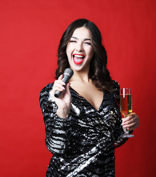 Young woman in black evening dress holding glass of champagne and microphone. - Fotó, kép