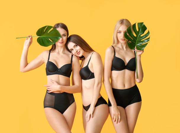 下着を着た美しい若い女性と色の背景に熱帯の葉を持つ - 写真・画像