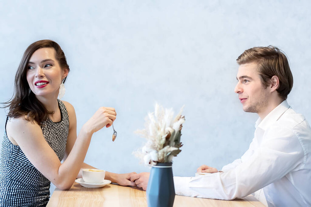 beautiful couple in a cafe at a table drinks coffee smiling at each other. space for text on the wall - Photo, Image