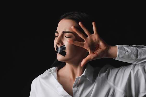 Scared female victim with taped mouth on dark background. Concept of violence - Фото, зображення