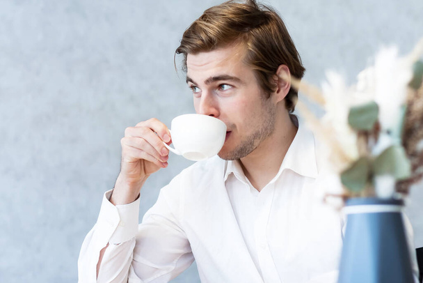 Handsome pensive male in white shirt looking away sitting at table in cafeteria thinking about plans, caucasian guy waiting for meeting in coffee shop dreaming about idea on leisure - Photo, image