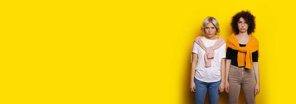 Two curly haired caucasian woman posing upset and sad on a yellow wall with free space - Foto, afbeelding