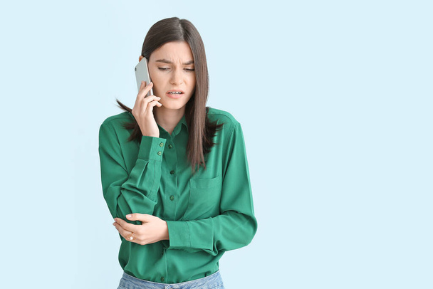 Troubled young woman with mobile phone on color background - Photo, Image
