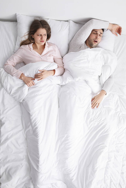 Młoda irytująca kobieta w łóżku z chrapiącym mężem w domu - Zdjęcie, obraz