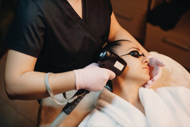 Gesichtshaarentfernung einer brünetten kaukasischen Frau mit modernen Geräten im Wellness-Salon - Foto, Bild