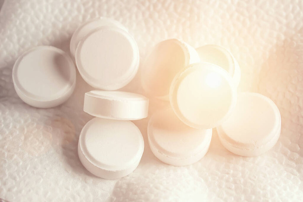 Λευκά χάπια βρίσκονται σε λευκό φόντο με φώτα bokeh. Εικόνα φόντου σε ιατρικά και φαρμακευτικά θέματα. Ιατρική, φαρμακείο και υγειονομική περίθαλψη. Ζωή χωρίς πόνο - Φωτογραφία, εικόνα