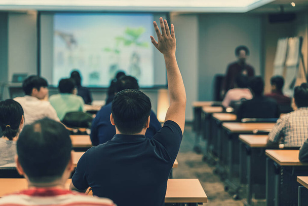 Rückansicht des Publikums in erhobener Hand zur Beantwortung der Frage im Besprechungsraum oder Konferenzsaal über einen asiatischen Redner auf der Bühne, Seminar-Business- und Bildungskonzept - Foto, Bild