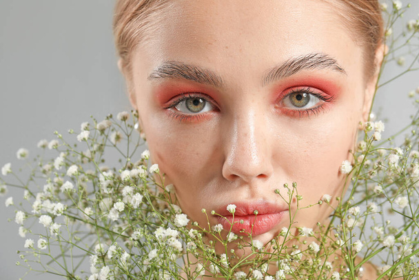 Young woman with beautiful makeup and flowers on grey background - Photo, Image