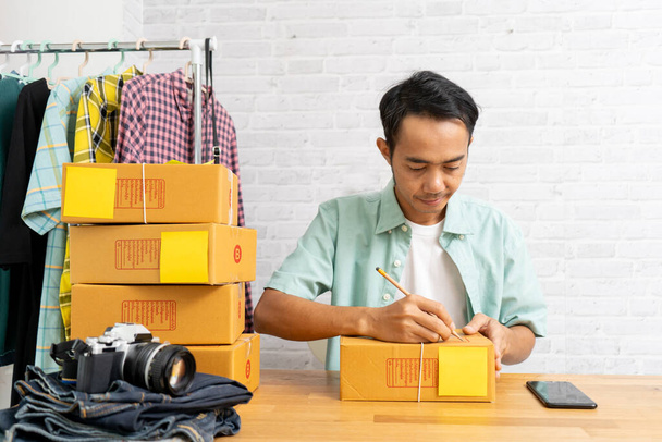 Asian man working at home office with carry brown parcel or cardboard boxes, e-commerce ideas concept - 写真・画像