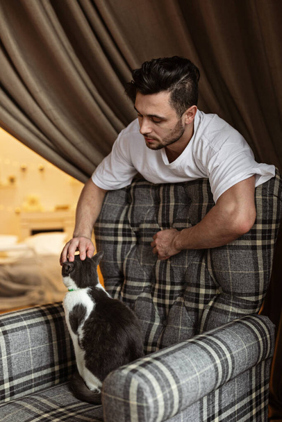 young man on the chair with his cat. Home pets. Lifestyle. Stay at home during coronavirus quarantine covid-19. - 写真・画像