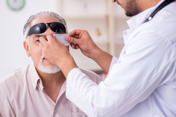 Oude blinde man op bezoek bij jonge mannelijke arts - Foto, afbeelding