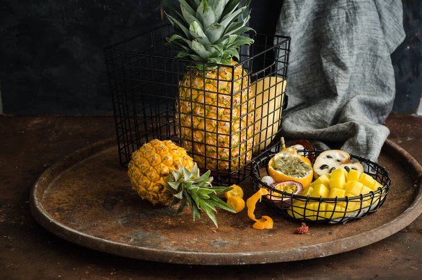 Still life with exotic fruits. Metal baskets with pineapple, mango, granadilla, passion fruit, mangosteen and kumquat. - Φωτογραφία, εικόνα