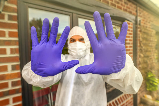 Een man met een beschermend masker en een hazmat pak die een waarschuwingsstopteken doet met zijn handen in handschoenen. Afsluiting en quarantaine. Coronavirus Covid-19-epidemie - Foto, afbeelding