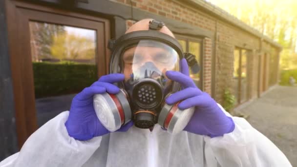 Homem coloca máscara respiradora completa e macacão hazmat branco durante coronavírus mundial covid-19 SARS-CoV-2 pandemia e bloqueio
. - Filmagem, Vídeo