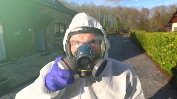 Mies yllään täydellinen hengityssuojain ja valkoinen hazmat coverall ja sininen käsineet aikana maailmanlaajuinen koronavirus covid-19 SARS-CoV-2 pandemia ja lukitus
. - Materiaali, video