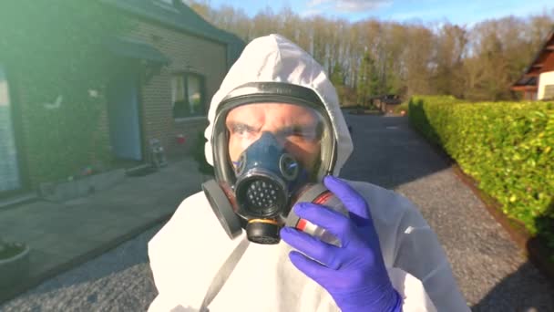 Muž s maskou plného dýchacího ústrojí a bílou kombinézou a modrými rukavicemi během celosvětové pandemie a uzamčení koronaviru SARS-CoV-2. - Záběry, video