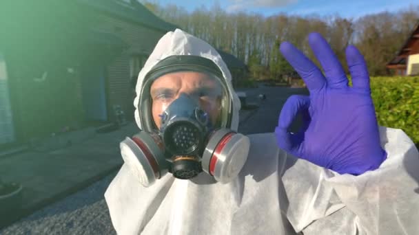 Mężczyzna w pełnej masce respiratora i białym okryciu ochronnym pokazuje znak ok podczas światowej pandemii i blokady koronawirusu covid-19 SARS-CoV-2. - Materiał filmowy, wideo