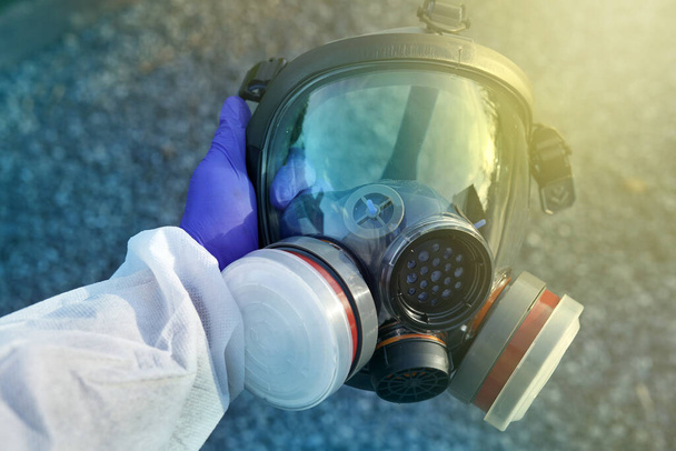 Rękawica w rękawicy trzymająca dużą maskę gazową przed zanieczyszczeniem Coronavirus Covid-19. Zamknięcie na pandemię wirusa SARS-CoV2. Specjalista od apokalipsy oddycha w masce antywirusowej i radiacyjnej. Odzież zagłady - Zdjęcie, obraz