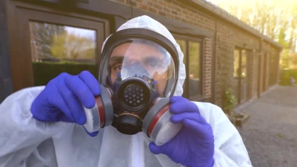世界中のコロナウイルスの間に完全なマスクと白いハズマットを脱ぐ男covid-19 SARSのCoV-2パンデミックとロックダウン. - 映像、動画