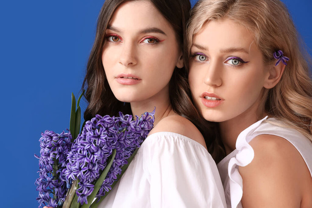 Όμορφες νεαρές γυναίκες με λουλούδια υάκινθος στο φόντο χρώμα - Φωτογραφία, εικόνα