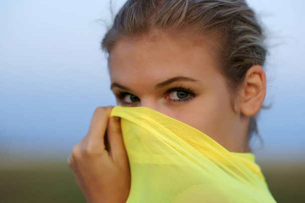  beautiful woman covering face with yellow chiffon scarf and posing outdoor  - Foto, afbeelding