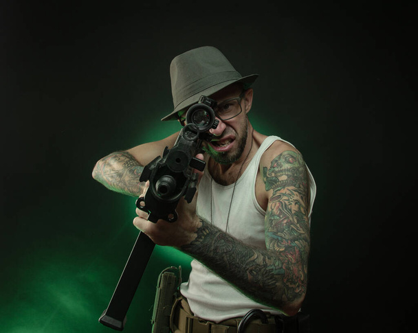 sportovní chlap s tetováním pózuje s automatickou puškou - Fotografie, Obrázek