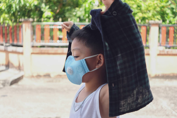 Corona Virüsü (Covid-19) salgınında evin dışına çıkmak için ceket ve mavi maske takan küçük çocuk. - Fotoğraf, Görsel
