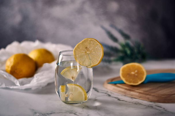 A shallow focus shot of pieces of lemonade inside the glass with two whole lemons on the paper and a bouquet of lavender in a blurred background - Foto, Imagen