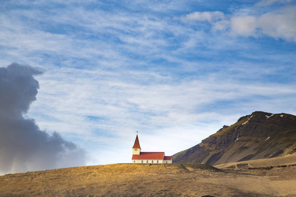 Um tiro largo de uma igreja vermelha e branca cercada por montanhas na Islândia
 - Foto, Imagem