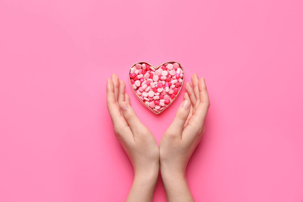 Mãos femininas e coração feito de pílulas em fundo de cor
 - Foto, Imagem