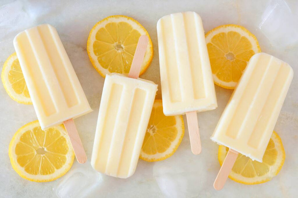 Healthy lemon yogurt popsicles with fresh lemon slices scattered on a white marble background - Foto, immagini