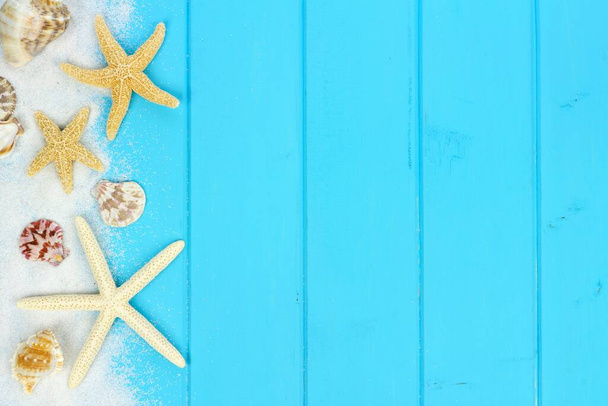 Summer side border of sand, sea shells and star fish on blue wooden background - Foto, Imagen