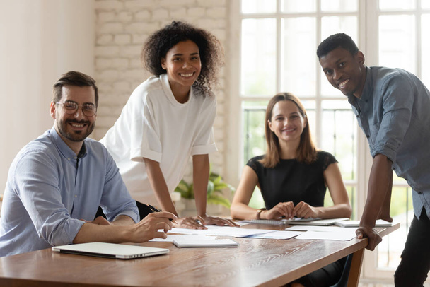 Fünf multiethnische Geschäftsleute versammeln sich lächelnd im Sitzungssaal und posieren für die Kamera - Foto, Bild