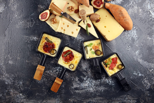 Delicious traditional Swiss melted raclette cheese on diced boiled or baked potato served in individual skillets with salami and potatoes - Photo, Image