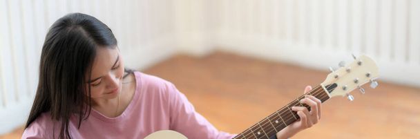 Cortada tiro de jovem estudante universitário de música feminina praticando guitarra enquanto sentado na sala de prática de música
 - Foto, Imagem