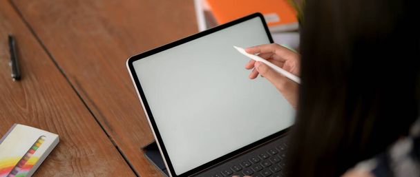 Recorte de la joven estudiante universitaria haciendo la tarea con la computadora portátil de pantalla en blanco en el escritorio de madera en la biblioteca
  - Foto, Imagen