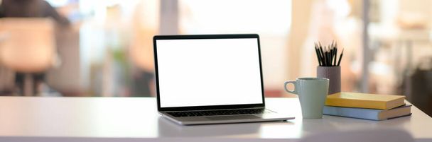Обрезанный снимок офисного стола с чистым экраном ноутбуком, канцелярскими принадлежностями, кофейной чашкой и копировальным местом на белом столе в стеклянной перегородке
 - Фото, изображение